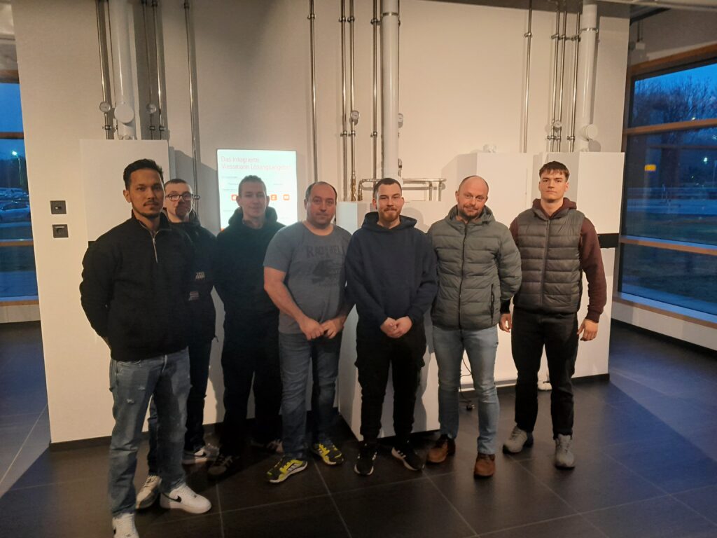 Menschen posieren in modernem Gebäude, Viessmann-Display im Hintergrund.